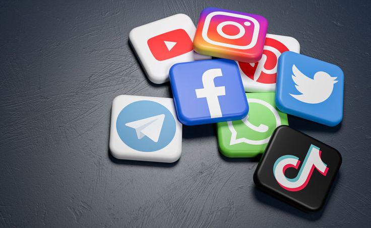 logos of the major social media and messaging sites (youtube, instagram, pinterest, twitter, facebook, whatsapp, telegram, tiktok) on a heap on a dark table. copy space web banner size
